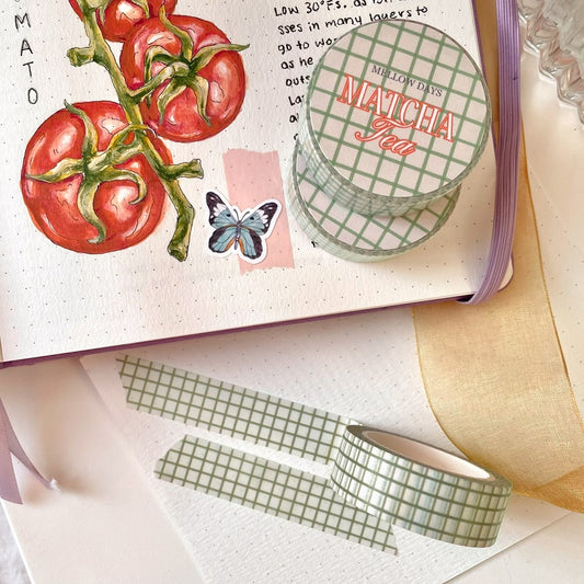 A roll of washi tape with a grid pattern in a sage green color, displayed on an open journal with bullet journal-style drawings and notes.