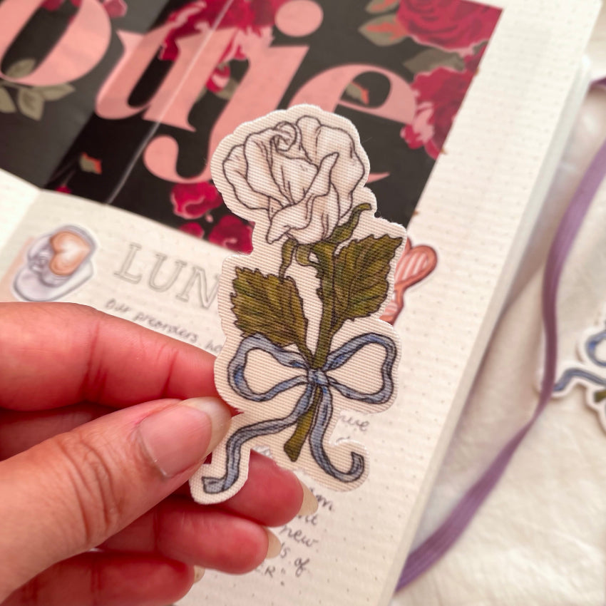 a fabric sticker that illustrates a single white rose tied with a blue ribbon bow 